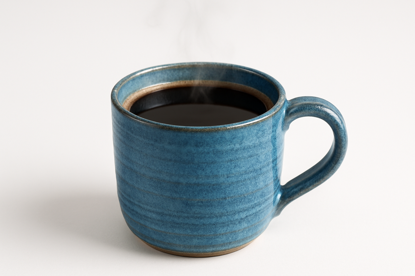 a blue pottery mug with coffee in it against a white background
